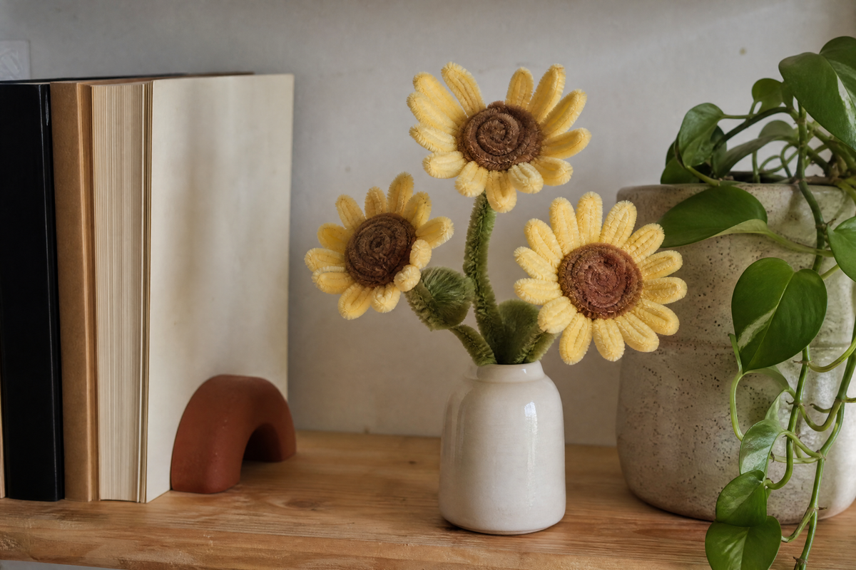 Florero con girasoles de limpiapipas en una repisa de casa